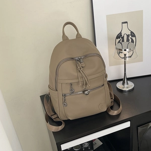 Close-up of khaki pebbled leather backpack with woven zipper pulls and metal ring detail