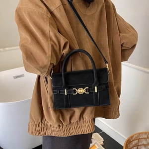 Detail of a black crossbody bag with gold crescent hardware on a person