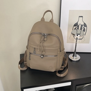 Close-up of beige leather backpack with tassel zippers and round logo detail