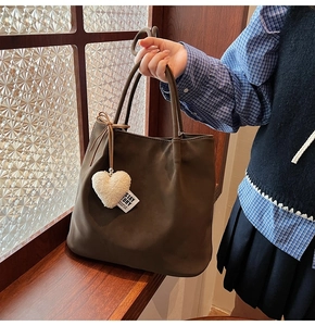 Detail of dark brown matte tote bag featuring a white plush heart charm and stay story label