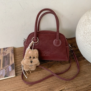 Dettaglio borsa bowling rosso scuro in ecopelle con logo in rilievo e ciondolo peluche