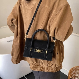 Detail of a matte black crossbody bag with gold metal buckle on a brown coat