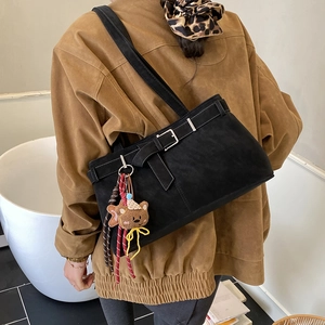 Detail of black suede tote bag with decorative buckle and plush bear charm on shoulder