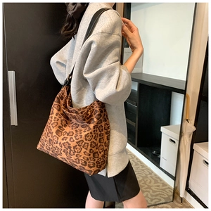 Side view of large leopard print shoulder bag with black strap on a female model