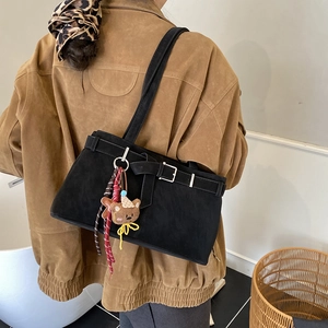Detail of black suede shoulder bag featuring metal buckle and cute bear charm accessory