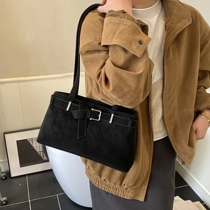 Detail of a black suede underarm bag with vintage buckle and shoulder strap worn by model