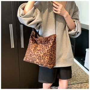 Detailed side view of large leopard print bucket bag with black strap on a shoulder