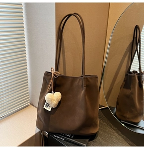Close-up of a dark brown tote bag with heart charm and 'STAY TRUE' label details