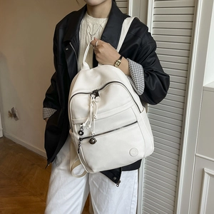 Detail of white lychee pattern leather backpack featuring multiple zippers and tassel charms