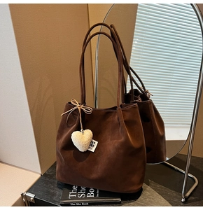 Detail of dark brown suede tote bag featuring a white plush heart charm and slim handles