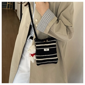 Detail of striped knit bucket bag with plush bear charm and egg tag on model