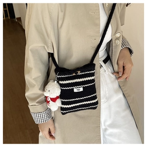 Detail of striped knit bucket bag featuring an egg label and red teddy bear charm
