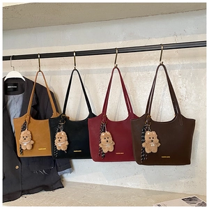 Detail view of four stylish tote bags in various colors with cute bear charms on a rack