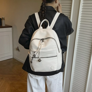 Close-up of white lychee leather backpack with metal ball charms and embossed logo