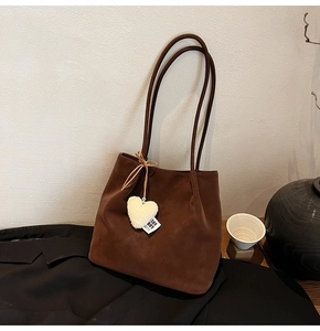 Detail of dark brown suede tote bag featuring a white plush heart charm on black fabric