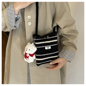 Detail of black and white striped knit crossbody bag with a plush bear charm and egg. logo