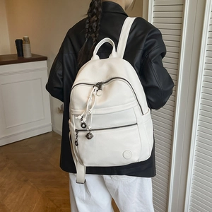 Detailed view of white faux leather backpack with litchi grain and metal pendant detail