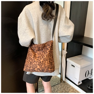 Detail view of large leopard print crossbody bucket bag with adjustable strap worn by model
