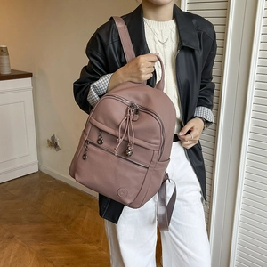 Detail of dusty rose leather backpack featuring tassel drawstring and round logo charm
