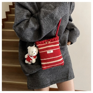 Close-up of striped knit bucket bag with a plush bear charm on grey knit dress