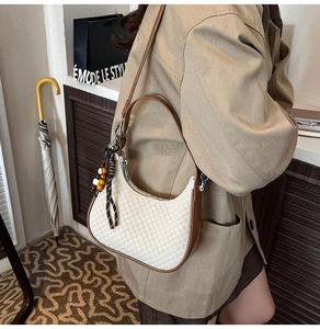 Side view of white woven crescent bag with brown trim and wooden bead charm detail