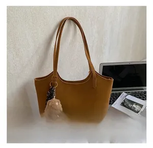 Detail of caramel brown tote bag with plush bear charm and striped scarf in office setting