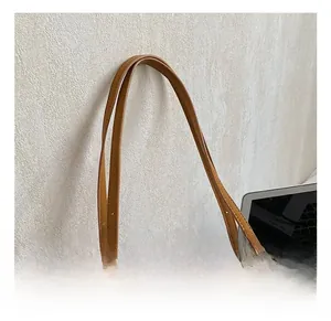 Detail of adjustable long slim handles and gold hardware on brown leather tote bag