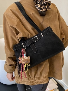 Chic black faux suede tote bag with a bear charm and strap buckle on a female model