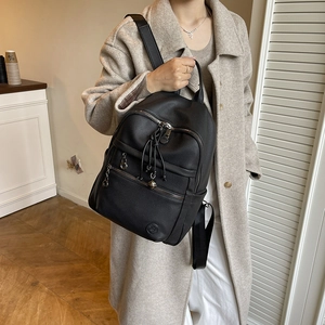 Detail of black lychee-textured leather backpack with decorative tassel and zipper