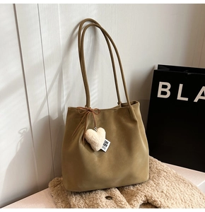 Detail of khaki suede tote bag featuring a white fuzzy heart charm and brown bow accessory