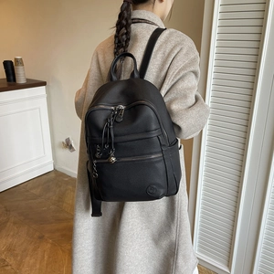 Detail of black pebbled leather backpack with silver zippers and elegant round pendant