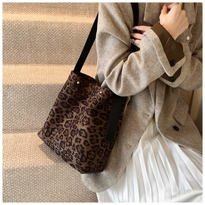 Close-up of leopard print bucket bag with wide black strap on a model wearing a beige blazer