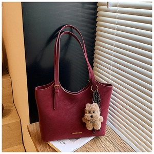 Detailed view of burgundy leather tote bag with adjustable straps and plush dog charm