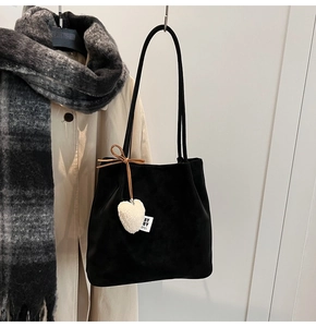 Detail of black suede tote bag featuring a white plush heart charm and side bow detail