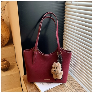 Retro burgundy leather tote bag with dog charm and silk scarf on a sunny wooden surface