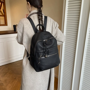 Detail of black pebbled leather backpack featuring metal rings and decorative tassels