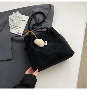 Detail of black suede tote bag featuring a white plush heart charm and brown bow accessory