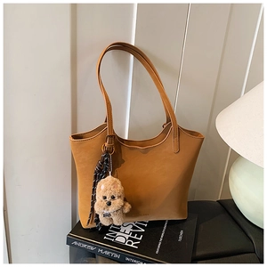 Detail of camel tote bag with plush dog charm resting on books against a striped wall