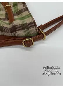 Close-up of adjustable brown leather shoulder strap with golden metal buckle on plaid bag