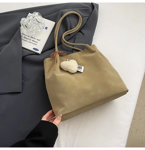 Close-up of khaki suede tote bag with heart charm and bow detail in a lifestyle setting