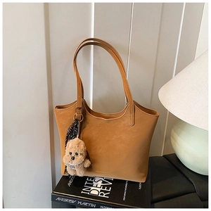 Brown leather tote bag with gold lettering and plush puppy charm on minimalist interior books
