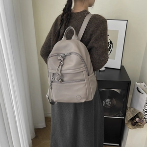 Close-up of beige leather backpack with silver zippers and knot tassel detail on model