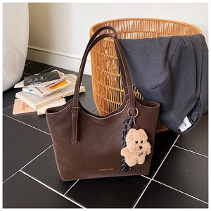 Detailed view of deep brown leather tote bag with golden logo and plush bear charm