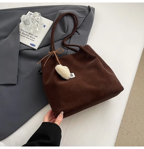 Detail of dark brown suede tote bag featuring a leather bow and plush heart charm