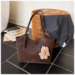 Detail of deep brown tote bag with FASHION & BAGS text and cute plush bear charm