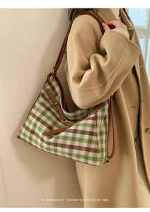 Close-up of green and brown plaid tote bag with leather strap on a model's shoulder