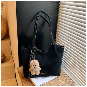Detail of a black matte tote bag with plush puppy pendant and brand logo engraving
