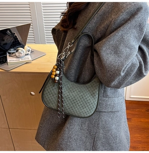 Detail of dark green woven crescent bag with wood bead tassel in minimalist office setting