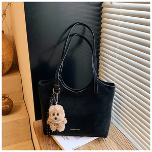 Detail of black tote bag with suede texture, gold lettering, and plush bear charm