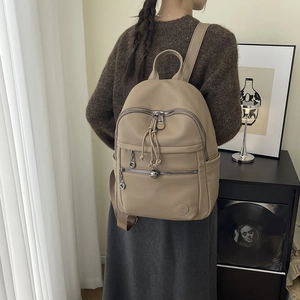 Detail of beige textured leather backpack with silver zippers and drawstring charm